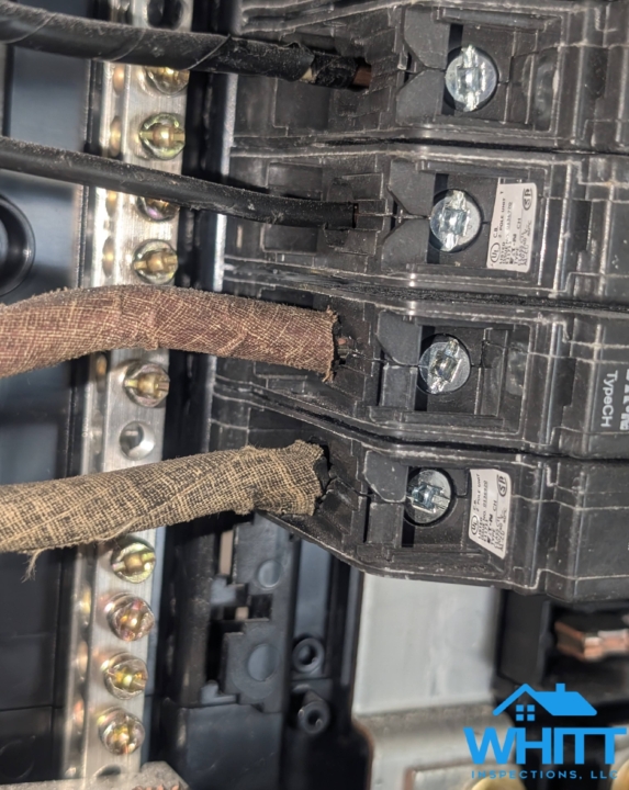 Close-up of frayed cloth electrical wiring connected to circuit breakers in an electrical panel.